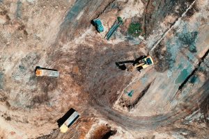 High-angle aerial view of construction site with earthmoving equipment and trucks.