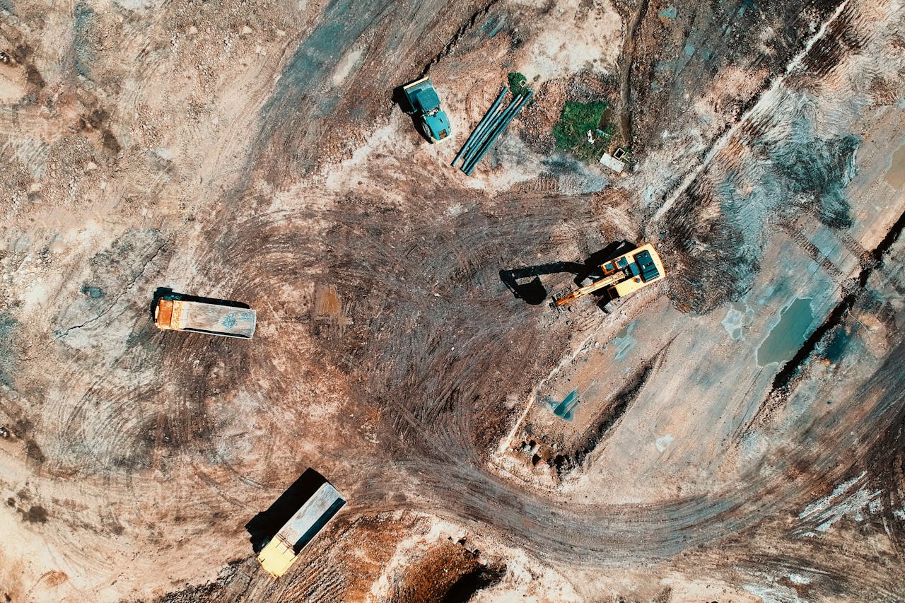 High-angle aerial view of construction site with earthmoving equipment and trucks.