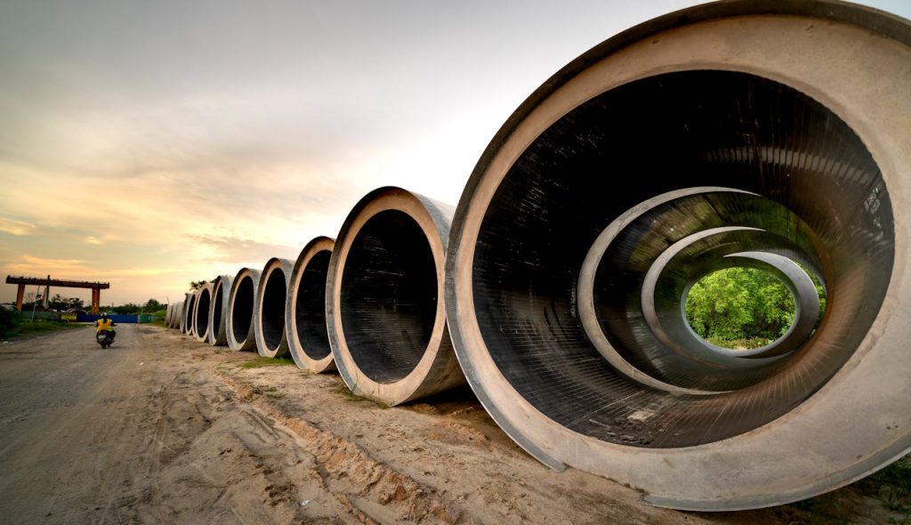 Massive concrete pipes aligned at a construction site during sunset, showcasing an industrial landscape.