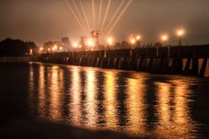 A scenic view of a brightly lit dam at night with reflections in the water.