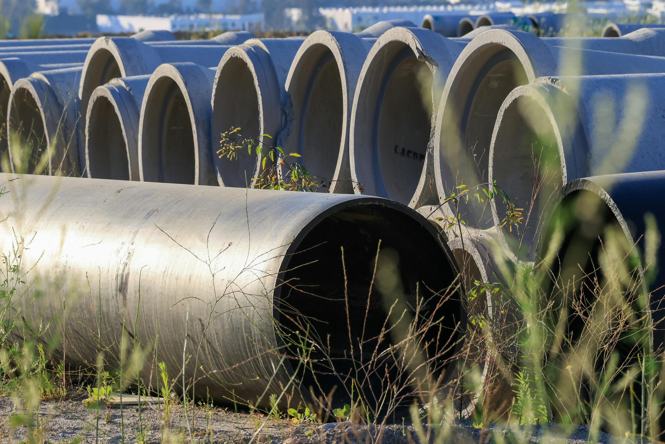 Stacked concrete pipes in an outdoor storage area surrounded by grass.