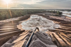 Drone shot of sand processing with flowing water and forest backdrop in Reads Landing, MN, at sunset.